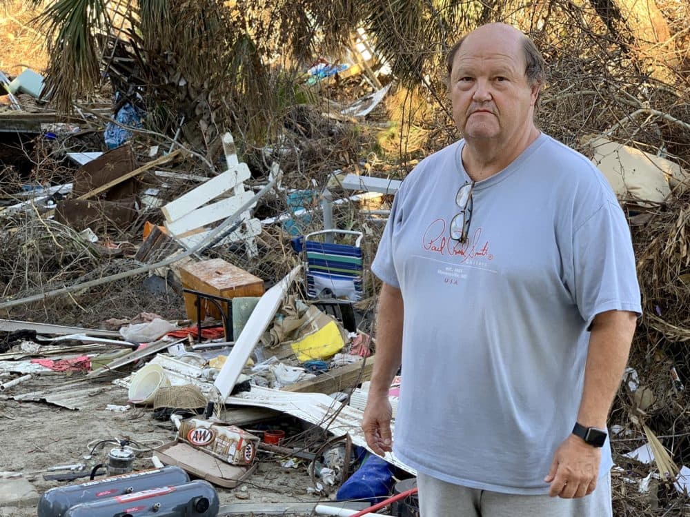 Troy Bryant in his backyard, with pieces of white picket fence strewn about among debris from his house and his neighbors'. (Chris Bentley/Here & Now)