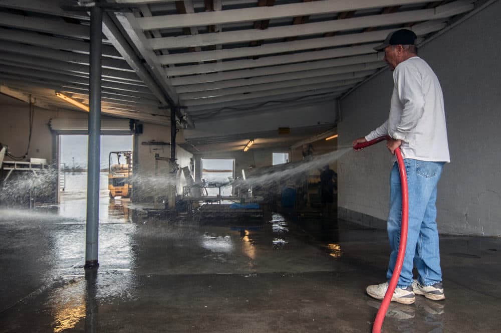 Walter Ward, co-owner of 13 Mile Seafood, washes away muck and debris from his oyster processing facility in Apalachicola, Fla. (Chris Bentley/Here & Now)