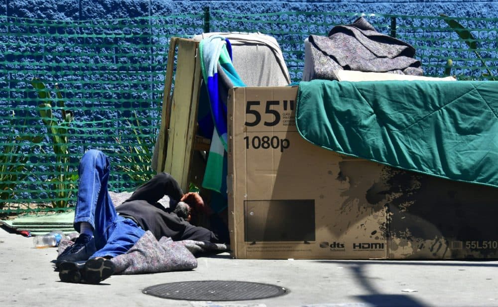 A homeless man sleeps beside his makeshift temporary shelter on a street in downtown Los Angeles in June 2018. (Photo by Frederic J. BROWN / AFP) (Photo credit should read FREDERIC J. BROWN/AFP/Getty Images)