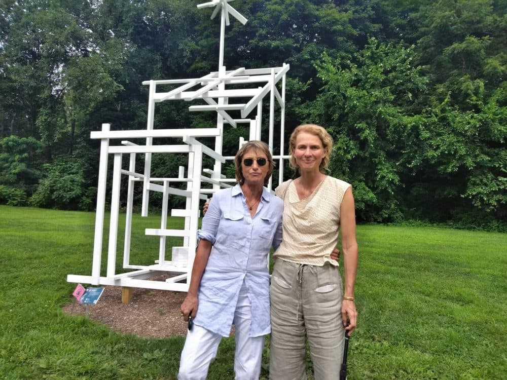 Curators Eva Fierst, left, and Sandy Litchfield stand with "Ghost Shed" by Tom Friedman. The sculpture is installed on land that used to be occupied by frat houses. (Jill Kaufman/NEPR)
