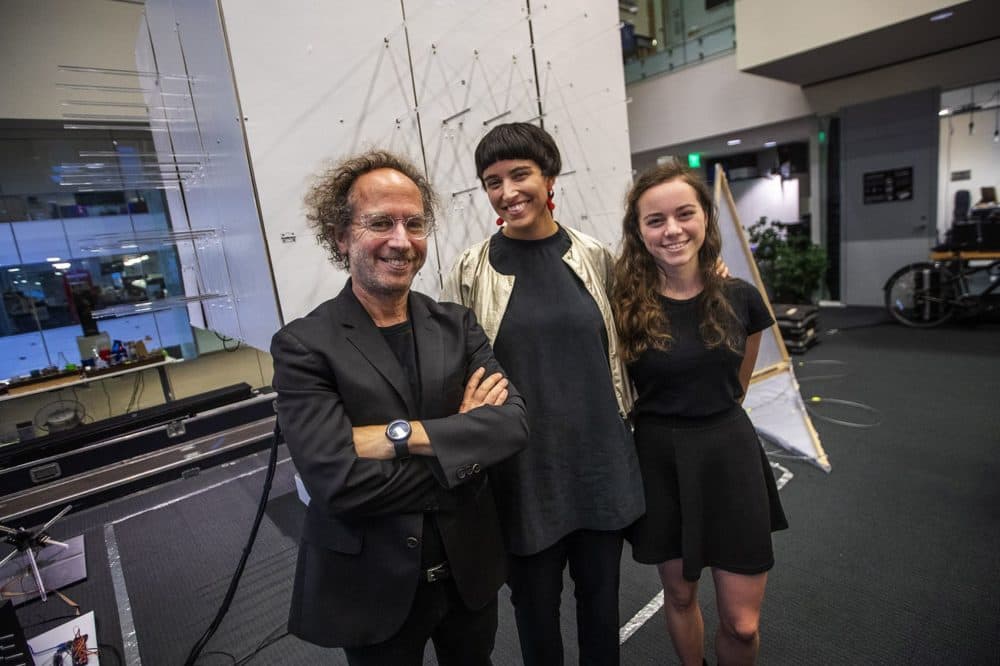 Tod Machover, director of MIT Media Lab's Opera of the Future group, Nicole L’Huillier and Hannah Lienhard stand in front of "The Cube," a small prototype of a room that changes shape in relation to sound and music being played through it. (Jesse Costa/WBUR)