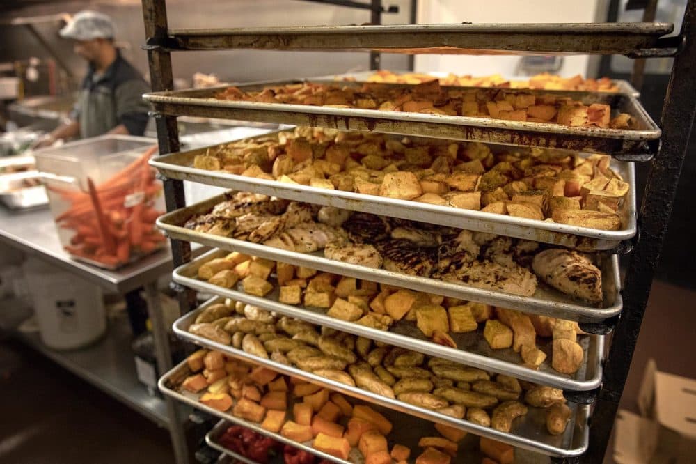 Trays of vegetables and chicken wait to be boxed at the Tuscan Market kitchen. (Robin Lubbock/WBUR)