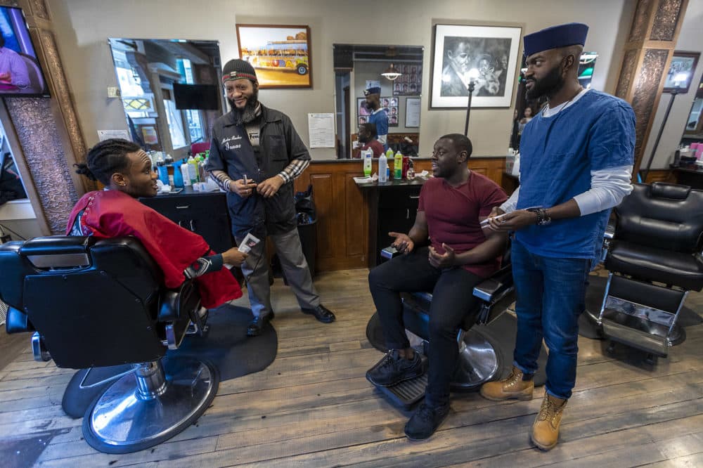 From right to left: Bright Genty and his father, master barber Isaac, speak with "Barber Shop Chronicles" actor Ekow Quartey and the production's writer Inua Ellams at Headlines Unisex Barbershop in Cambridge. (Jesse Costa/WBUR)