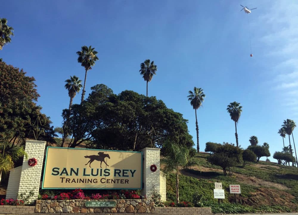 In this Dec. 8, 2017, file photo, a helicopter prepares to make a water drop over the San Luis Rey Training Center, where thoroughbreds are housed and trained, in Bonsall, Calif. (Amanda Lee Myers/AP)
