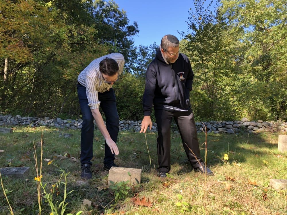 Historian Alex Green, left, and Gann Academy teacher Yoni Cadden point to a grave marker in Waltham's Metfern Cemetery (Eve Zuckoff/WBUR).