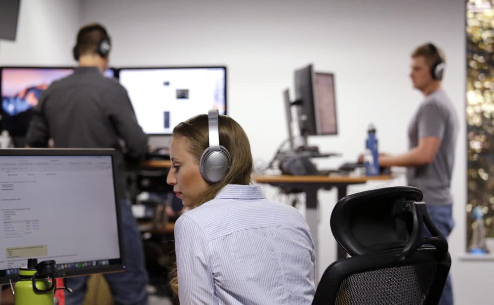 Meg Dowaliby, along with her colleagues behind, wears Bose noise-canceling headphones, a perk of her job, as she works at her computer at Geniuslink in Seattle. (Elaine Thompson/AP)