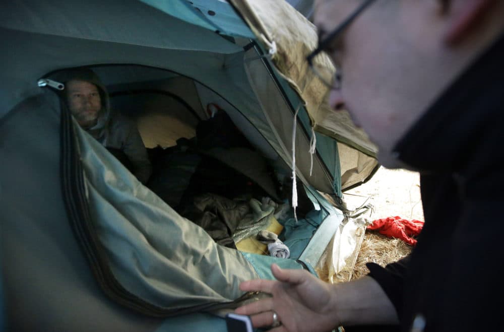 Worcester police officer Angel Rivera, right, asks Brian Pickering, left, if he has been tested for for Hepatitis A at the entrance to a tent where Pickering spent the night in a wooded area, in Worcester, Mass. (Steven Senne/AP)