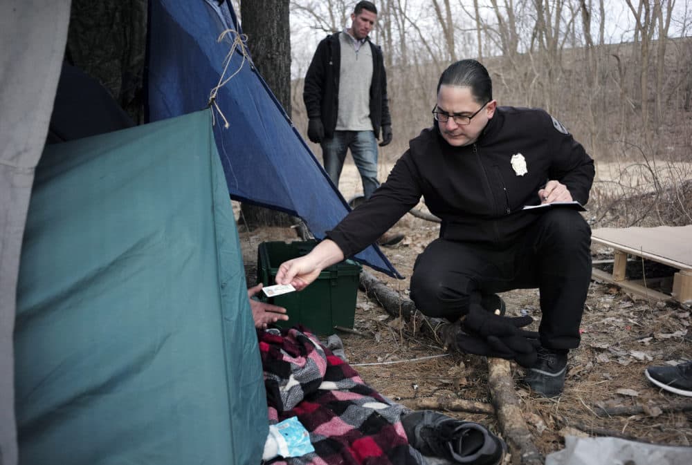Worcester police officer Angel Rivera, right, returns a license to an unidentified man as Rivera asks if he has been tested for Hepatitis A at the entrance to a tent where the man spent the night in a wooded area, in Worcester, Mass. (Steven Senne/AP)