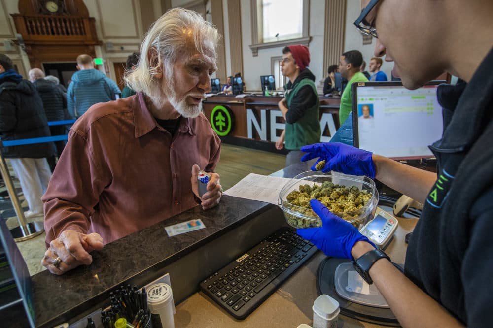 NETA associate Kyle Chambers shows patient Richard Morse a plastic container filled with the Blackwater OG strain of cannabis flower at the NETA marijuana dispensary in Brookline Village. (Jesse Costa/WBUR)