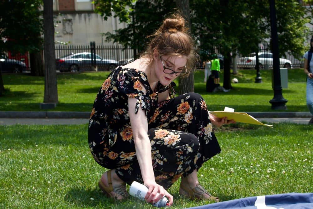 Izzy Goodrich, 15, of Boston, uses spray paint to add depth and texture to the whale's cloth border. (Miriam Wasser/WBUR)