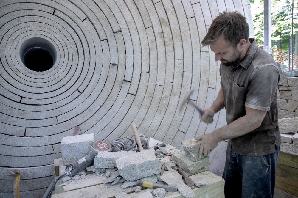 Adrian Blant, a dry stone waller from Yorkshire, U.K., works on a stone for "Watershed" at deCordova. (Robin Lubbock/WBUR)