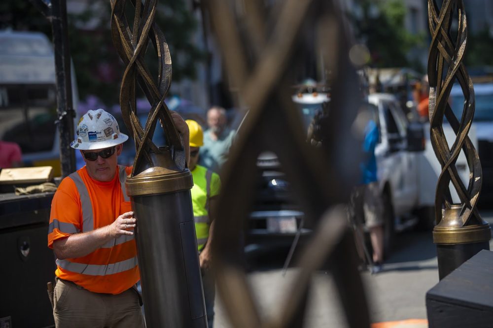 Installation worker Paul Beaulieu maneuvers an airborne spire suspended by a crane toward the location of its mount. (Jesse Costa/WBUR)