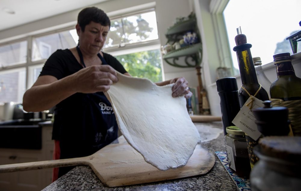 After rolling out the dough, Kathy Gunst moves the dough onto a pizza peel before applying the toppings for her white clam pizza. (Jesse Costa/WBUR)