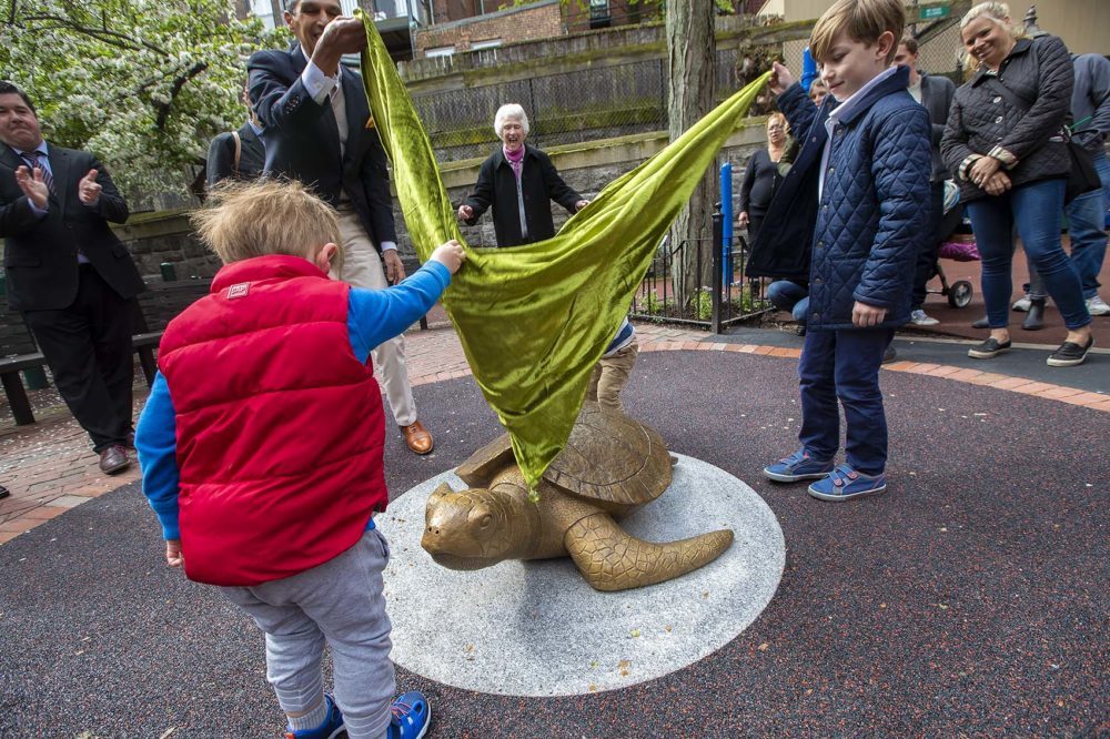 Sculptor Nancy Schön cheers from behind as children help unveil the "Myrtle the Turtle" sculpture in May. The sculpture is now being moved to prevent children climbing on it. (Jesse Costa/WBUR)