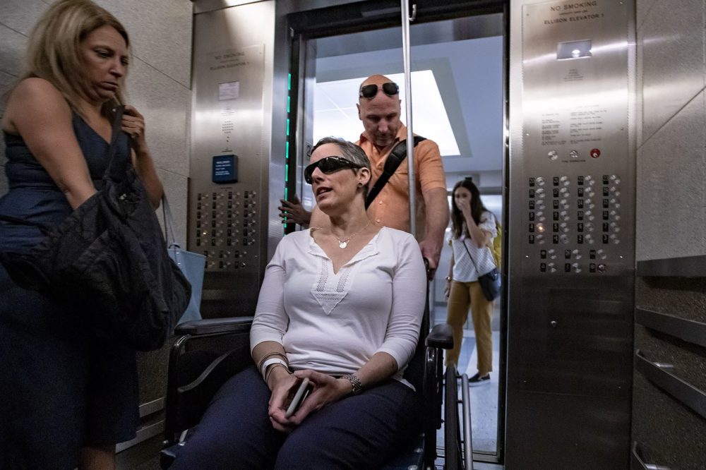Lauren Corduck gets wheeled into an elevator by her husband Robb at Massachusetts General Hospital on her way to her sixth course of treatment for ovarian cancer. (Jesse Costa/WBUR)