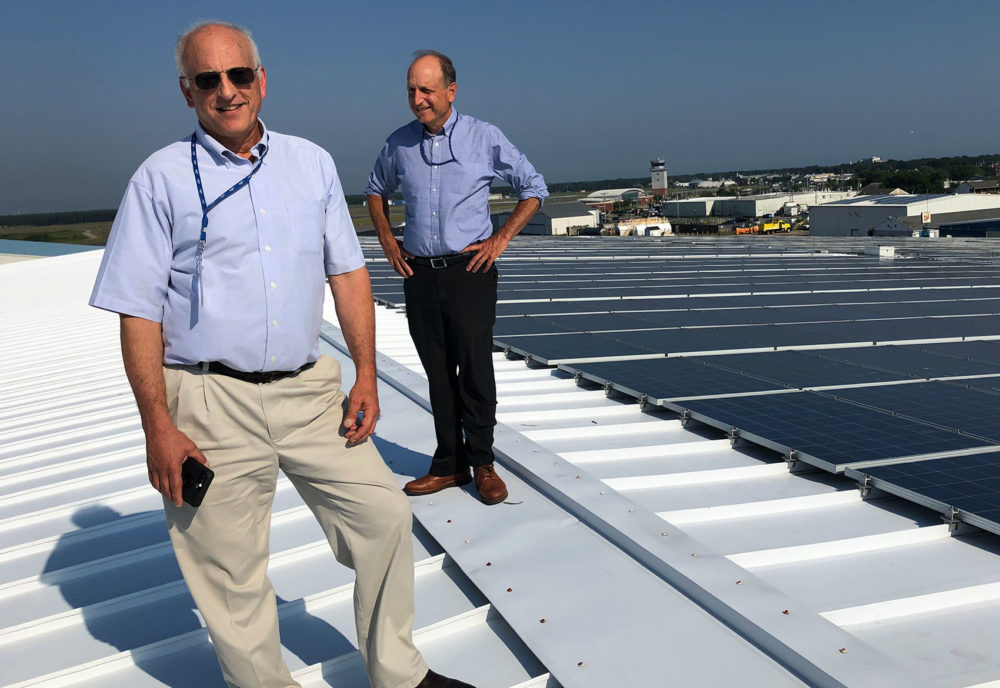 Cape Air founder and CEO Dan Wolf, right, and his brother Jim, the airline's director of sustainability, stand next to Cape Air's own solar array. (Bruce Gellerman/WBUR)