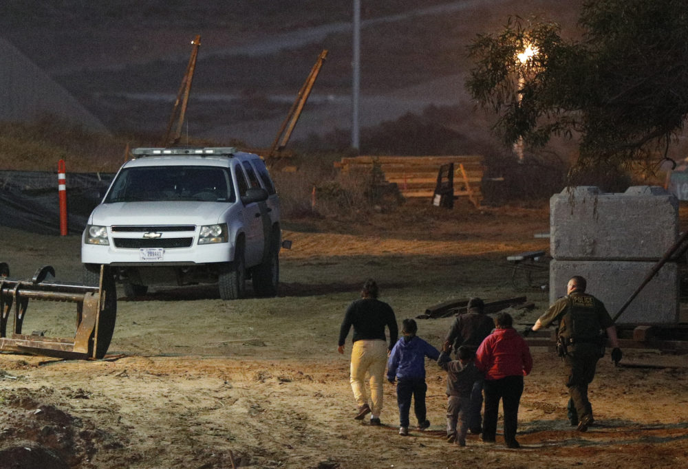 In this Dec. 3, 2018 file photo, migrants are escorted by a U.S. Border Patrol agent as they are detained after climbing over the border wall from Playas de Tijuana, Mexico, to San Ysidro, Calif. (Rebecca Blackwell/AP)