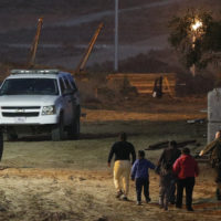 In this Dec. 3, 2018 file photo, migrants are escorted by a U.S. Border Patrol agent as they are detained after climbing over the border wall from Playas de Tijuana, Mexico, to San Ysidro, Calif.  (Rebecca Blackwell/AP)