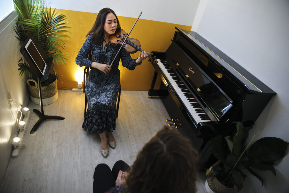 Jean Huang performs for Kristina Carroll in a brightly colored shipping container in the middle of Chinatown. (Erin Clark for WBUR)