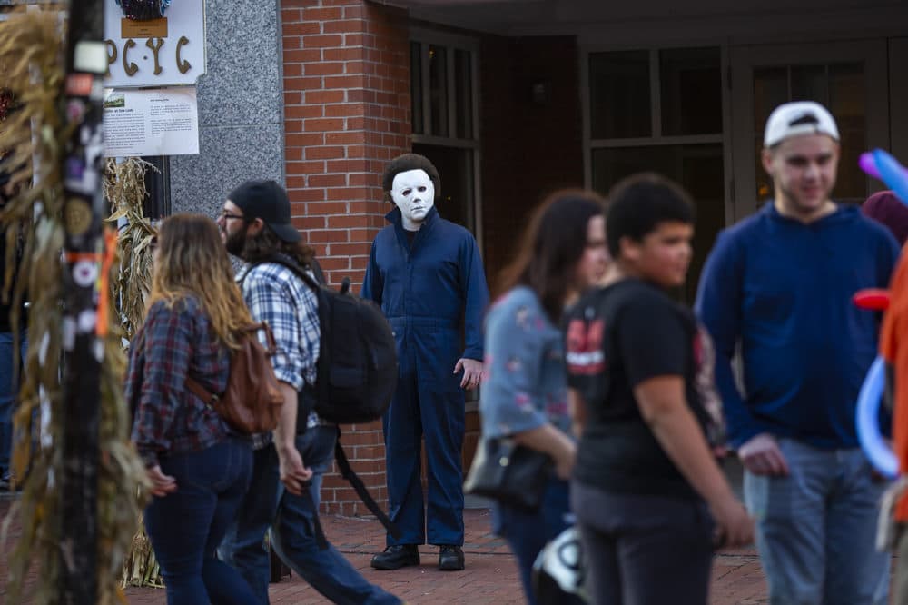 A street performer portraying the role of Michael Myers from the horror classic “Halloween” stands amid visitors to Salem along Essex St. (Jesse Costa/WBUR)