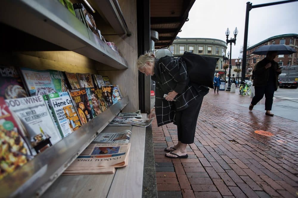 A woman looks at the cover of the New York Daily News outside the newsstand, which once was brimming with publications. (Jesse Costa/WBUR)