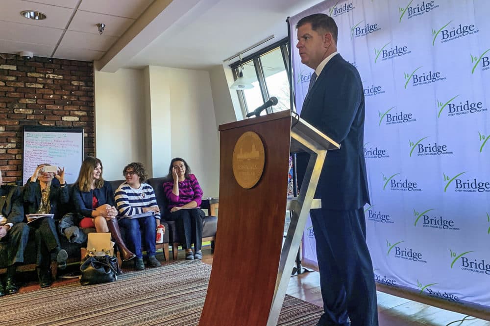 Boston Mayor Marty Walsh speaks to a crowd of people about youth homelessness on Thursday, Nov. 21. Nick Shoults sits along the side, third chair from the left. (Steve Brown/WBUR)