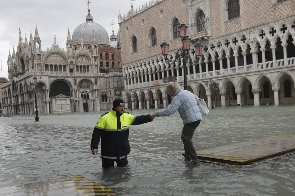A city worker helps a woman who decided to cross St. Mark square on a gangway, in spite of prohibition, in Venice, Italy, Sunday, Nov. 17, 2019. (Luca Bruno/AP)