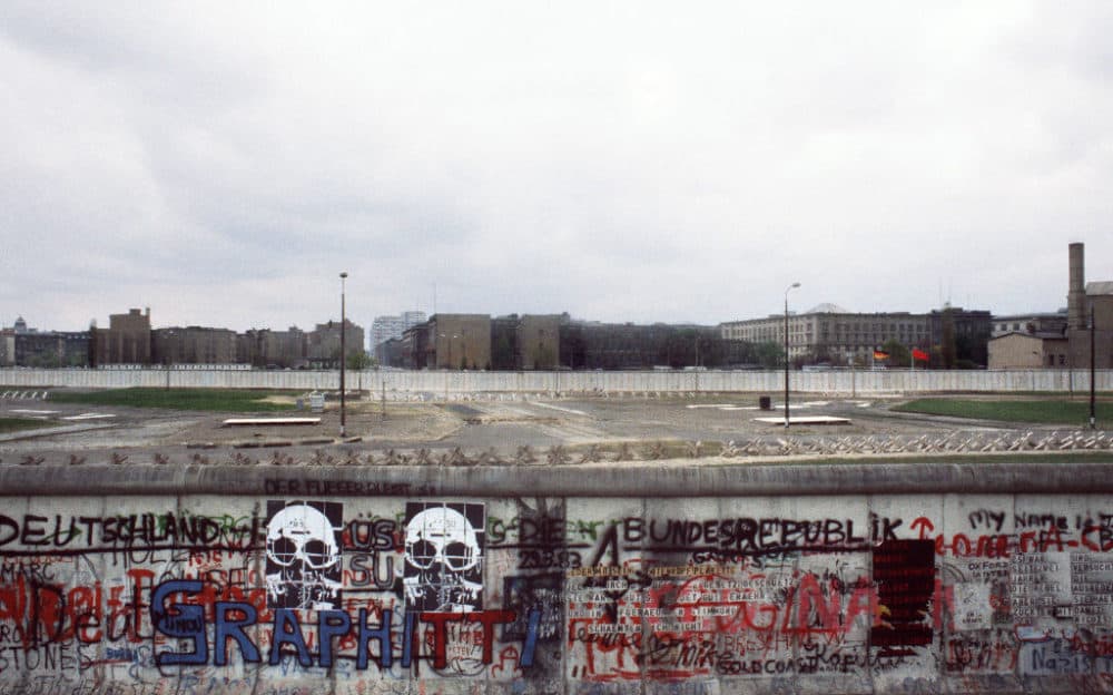 Various graffiti is painted on the Berlin Wall on the West Berlin side in April 1984 while East German and Soviet flags (R) fly on the other side of the East Berlin no-mans-land spiked with anti-tanks traps. (Joel Robine/AFP/Getty Images)