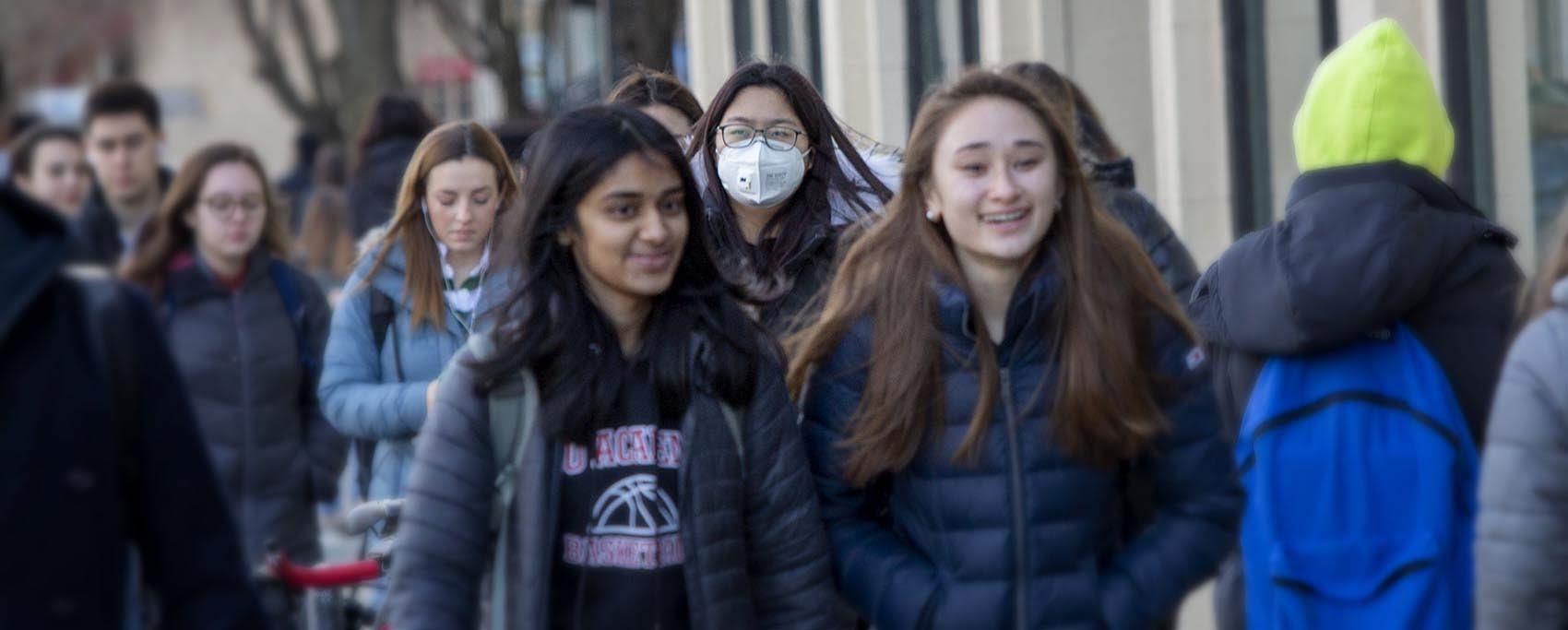 A woman wears a mask as she walks along on a busy Boston sidewalk. (Robin Lubbock/WBUR)