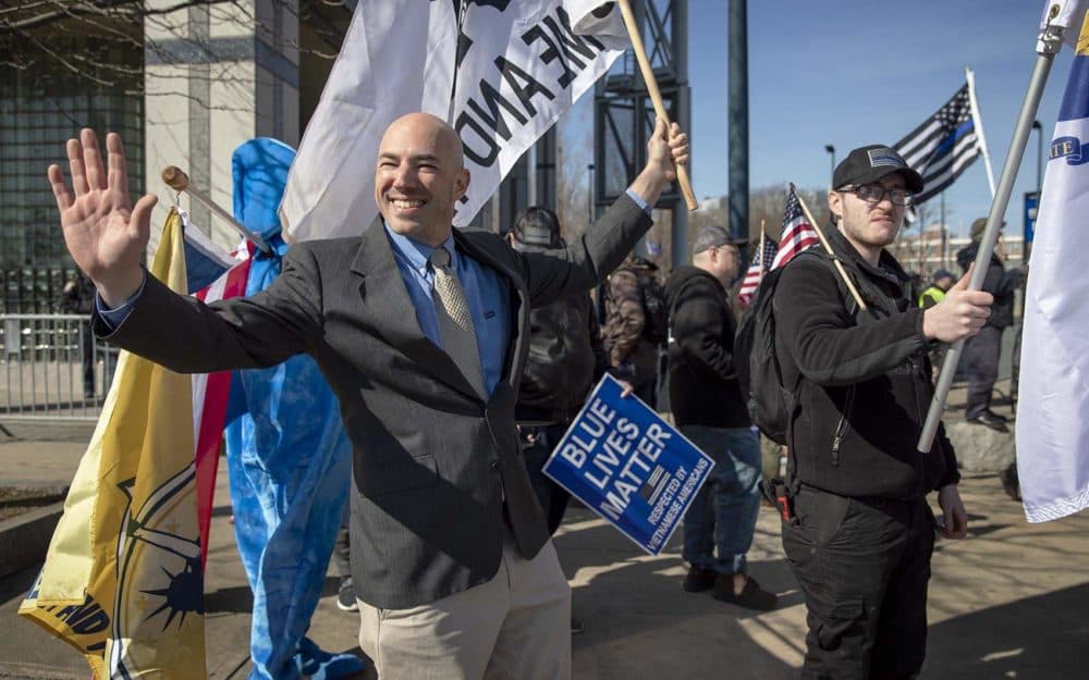 Samson Racioppi, one of the leaders of Super Happy Fun America, waves at passing cars during a rally outside Boston Police Headquarters. (Robin Lubbock/WBUR)