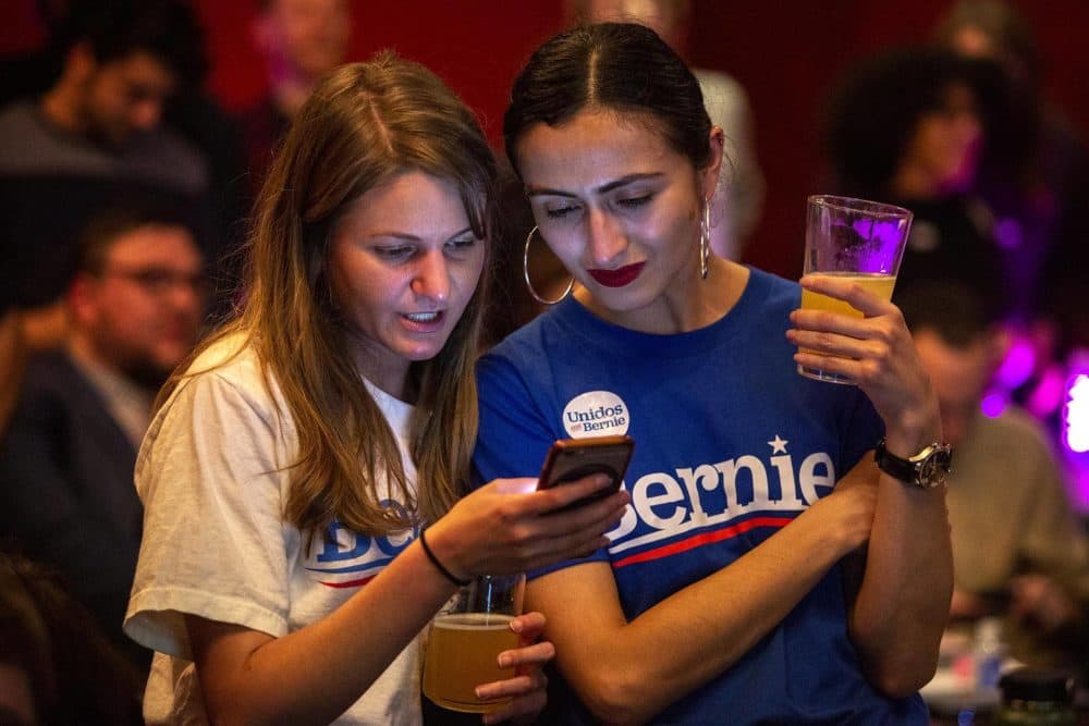 Bernie supporters Grace Holley and Luz Perez look over a phone as returns come in for Super Tuesday. (Robin Lubbock/WBUR)