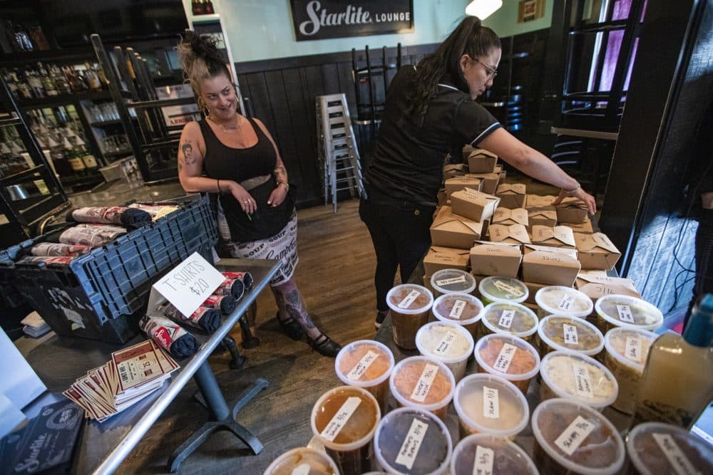 Staff at Trina’s Starlite Lounge in Somerville put meals out on a table for patrons to pick up at the front door. All the food prepared was made with food the restaurant would have discarded due to the the state's order beginning March 17, preventing people from gathering at bars and restaurants, a move to reduce the risk of spreading the coronavirus. All the proceeds of the sales will go to their staff. (Jesse Costa/WBUR)