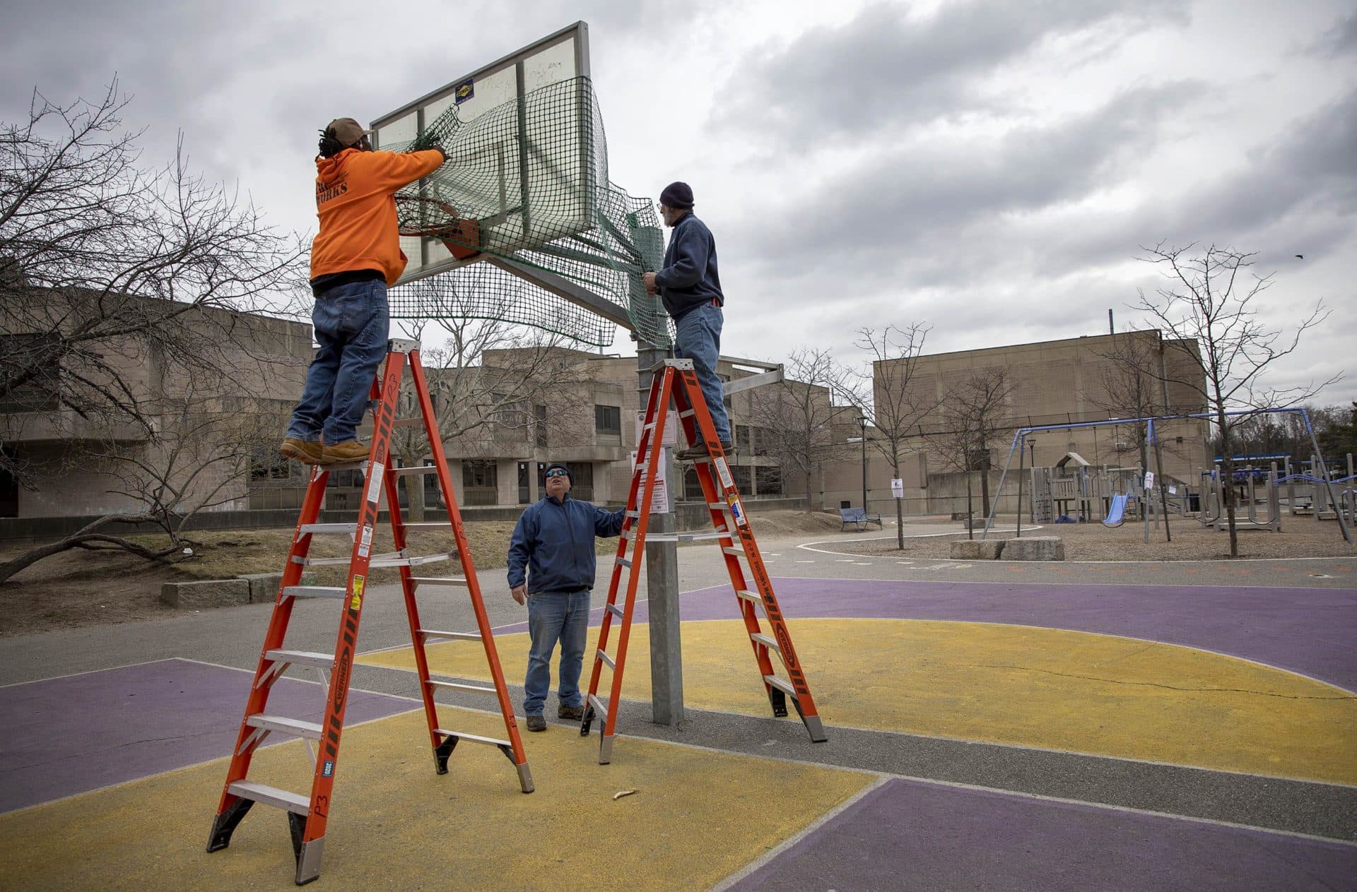 Cambridge Department of Public Works staff wrap a basketball hoop in plastic fencing, to discourage team games, as state and city governments attempt to slow the spread of the coronavirus. (Robin Lubbock/WBUR)