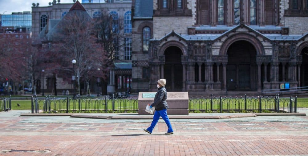 A woman wearing a face mask walks through a virtually empty Copley Square. (Jesse Costa/WBUR)