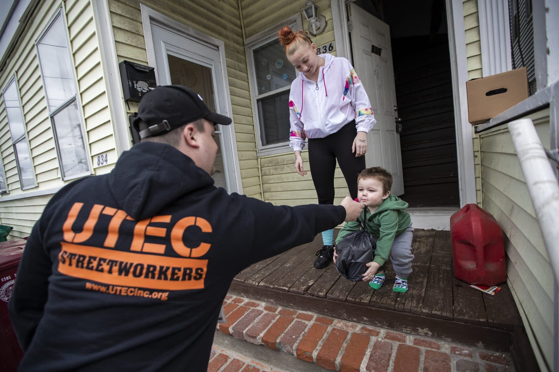James O’Keefe hands a bag of supplies to one-and-a-half year old Joshua Babbin while his mother Erin watches. (Jesse Costa/WBUR)
