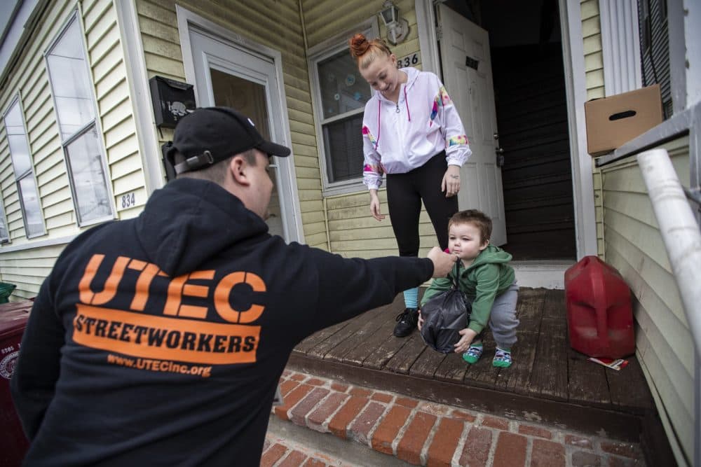 James O’Keefe hands a bag of supplies to one-and-a-half year old Joshua Babbin while his mother Erin watches. (Jesse Costa/WBUR)