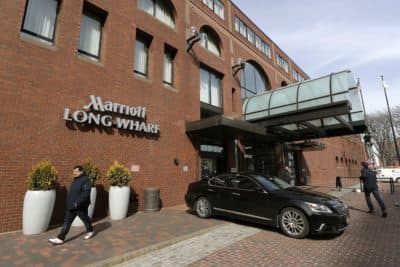People walk outside the Marriott Long Wharf hotel, March 11, in Boston, the site of the Biogen conference that was held at the hotel in late February 2020. (Steven Senne/AP)