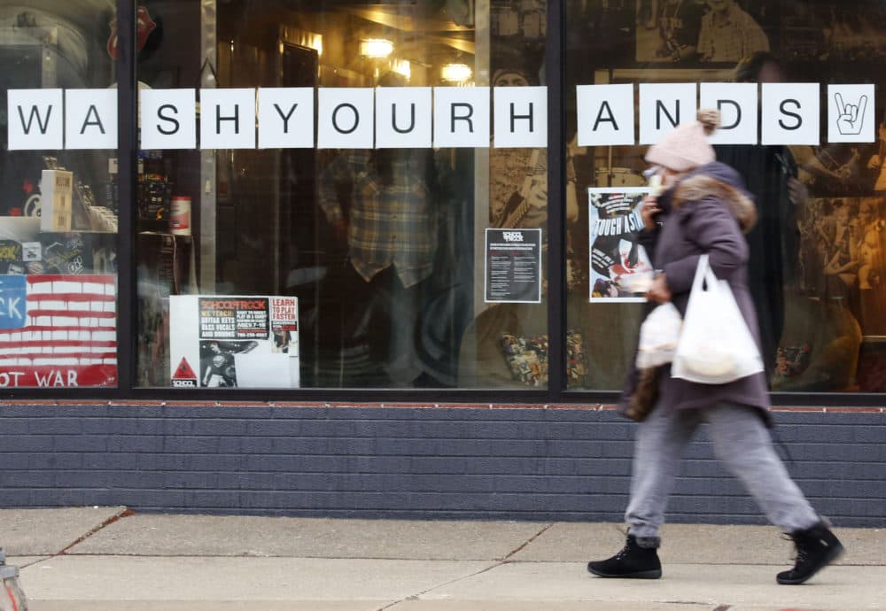 In this March 19, 2020, photo, a woman in a face mask walks past a "Wash Your Hands" sign after buying groceries in Oak Park, Ill., before a two-week "shelter in place" order goes into effect. (Martha Irvine/AP)
