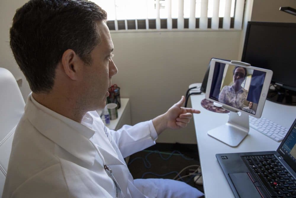 The coronavirus pandemic has prompted more people in Massachusetts to turn to telemedicine. Here, Dr. Philip Ciampa from the Atrius Health innovation center (left) talks with a colleague (at the top of the screen), in a demonstration of a "virtual visit." (Robin Lubbock/WBUR)