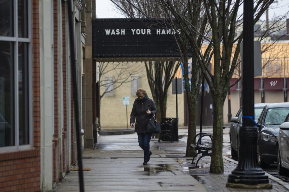 A woman walks past a closed Norwood Cinema where the marquee reads "Wash your hands." (Jesse Costa/WBUR)