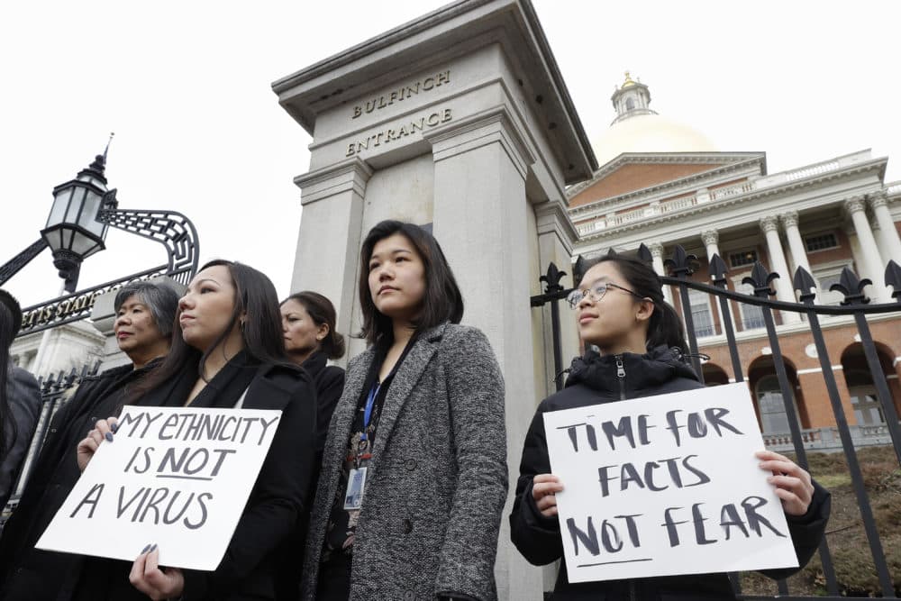 Jessica Wong, of Fall River, Mass., front left, Jenny Chiang, of Medford, Mass., center, and Sheila Vo, of Boston, from the state's Asian American Commission, stand together during a protest, Thursday, March 12, 2020, on the steps of the Statehouse in Boston. (Steven Senne/AP)
