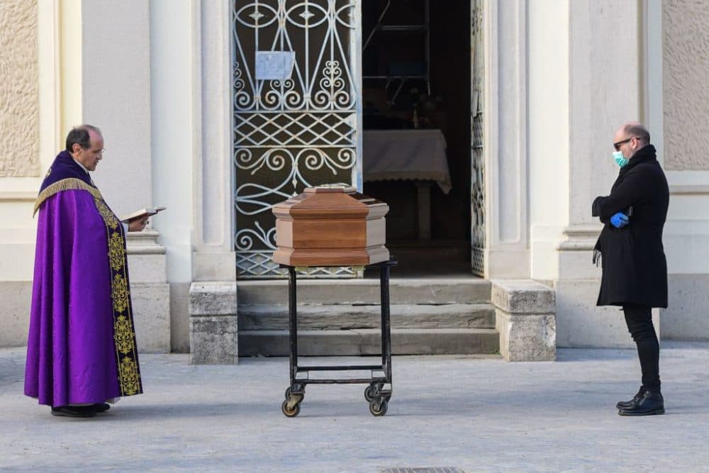 A man wearing a face mask stands by the coffin of his mother as a priest reads prayers. (Piero Cruciatti/AFP/Getty Images)