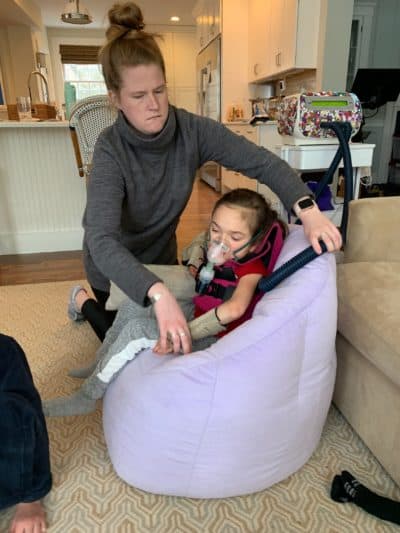 Aide Kendra Sloan positions Harper in a chair with a nebulizer. (Photo courtesy Dawn Oates)
