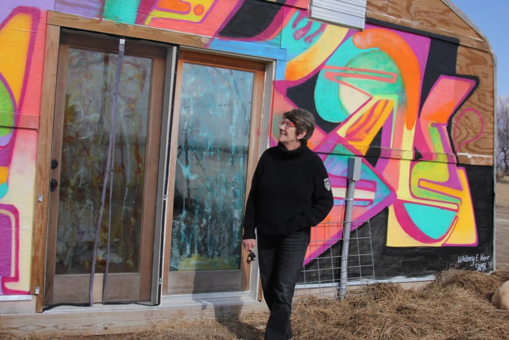 Patti O'Malley next to one of the greenhouses on her property (Yasmin Amer/WBUR)