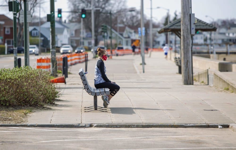 A woman, wearing a mask against COVID-19, looks out to sea across Wollaston Beach. (Robin Lubbock/WBUR)