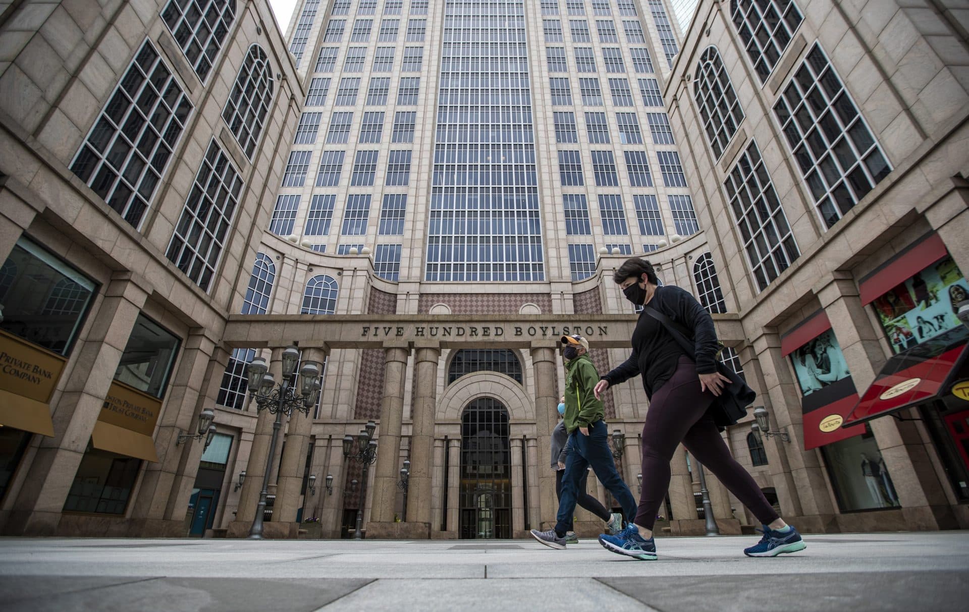 Three people walk past 500 Boylston St. on the first day face coverings are required to be worn in the state. (Jesse Costa/WBUR)