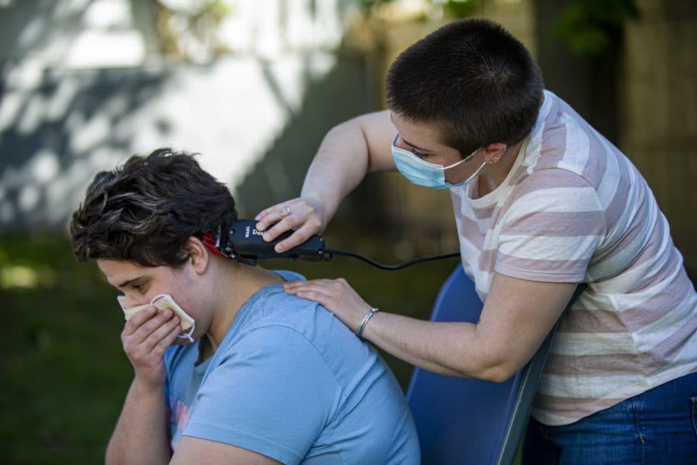 Neighbor Lauren Keisling trims the hair of Ryley Copans in their backyard with a brand new pair of clippers. (Jesse Costa/WBUR)