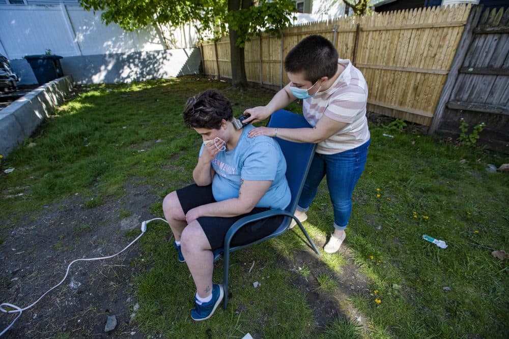 Neighbor Lauren Keisling trims the hair of Ryley Copans in their backyard with a brand new pair of clippers. (Jesse Costa/WBUR)
