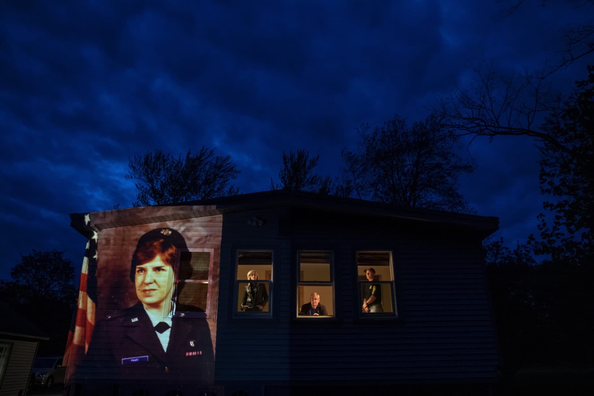An image of veteran Constance "Kandy" Pinard is projected onto the home she grew up in with her sister, Tammy Petrowicz, left, and brothers, Paul, center, and Brian Driscoll in Florence, Mass. (David Goldman/AP)