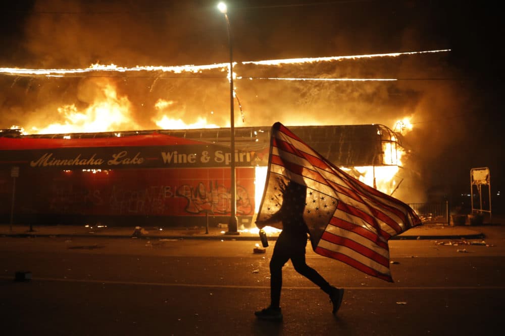 A protester carries a U.S. flag upside down, a sign of distress, next to a burning building Thursday, May 28, 2020, in Minneapolis. Protests over the death of George Floyd, a black man who died in police custody Monday, broke out in Minneapolis for a third straight night. (Julio Cortez/AP)
